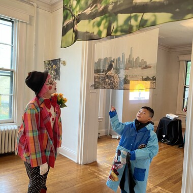 An NYC Audubon volunteer engages with a young Island visitor below the work of 2023 AiR Carolyn Monastra.